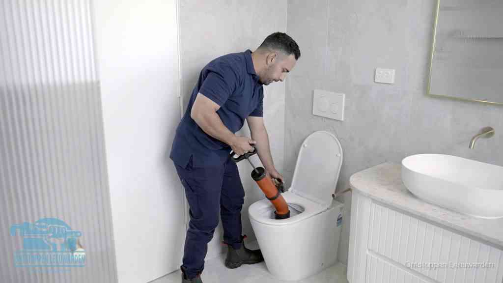 Een monteur buigt over een wandcloset en duwt met de hand een persluchtontstopper in de toiletpot om de verstopping handmatig los te maken in Leeuwarden