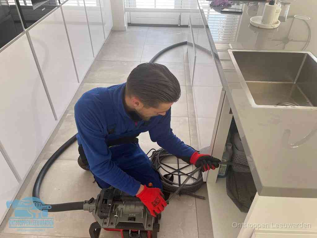 Een monteur ontstopt de keukenafvoer onder de spoelbak met een elektrische veermachine in Leeuwarden