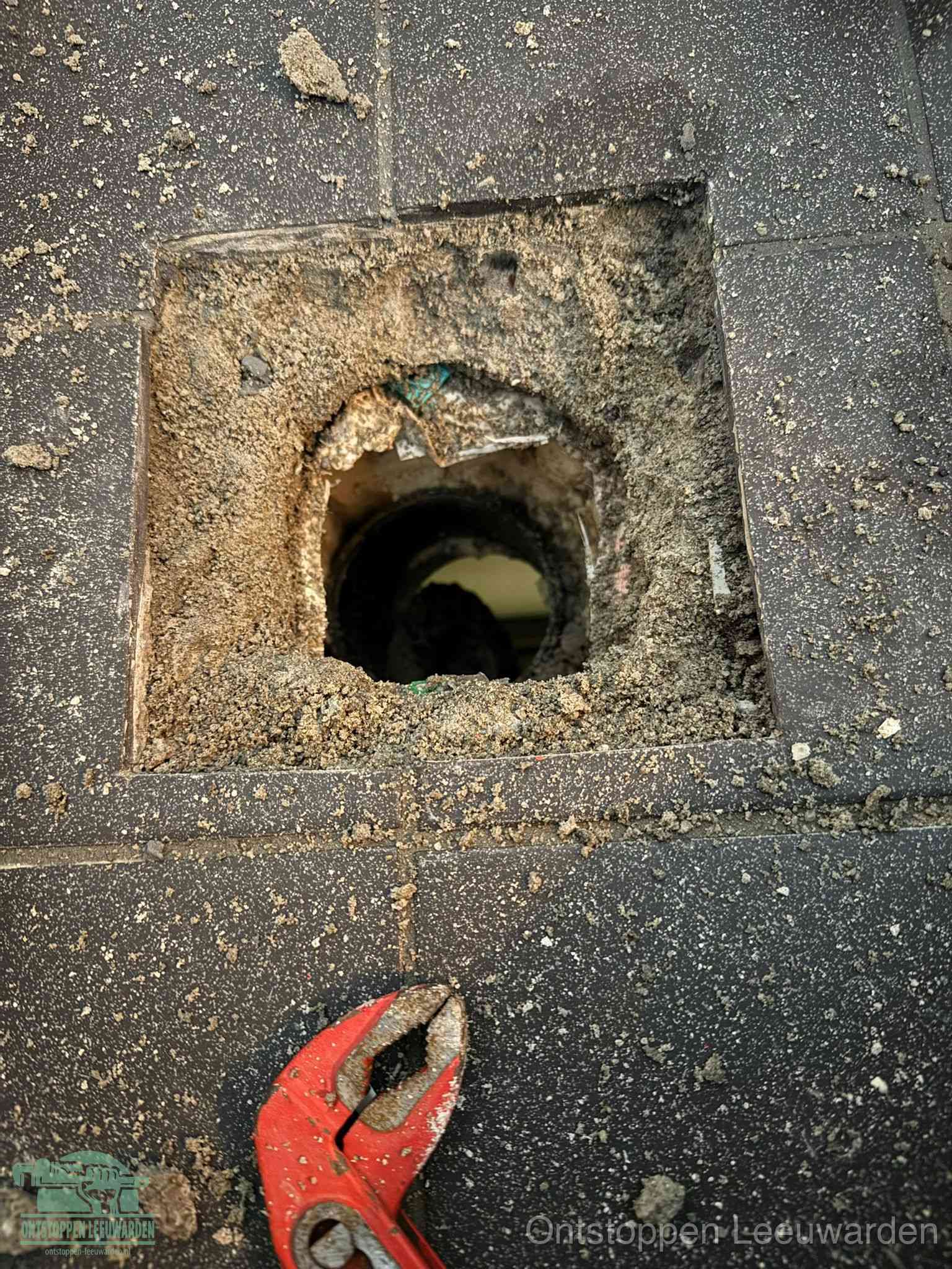 Een geopend rioolputje in een betontegelvloer met losgemaakt rooster en een zichtbare ronde afvoerbuis, het achterhalen waar de afvoerverstopping zit in Leeuwarden