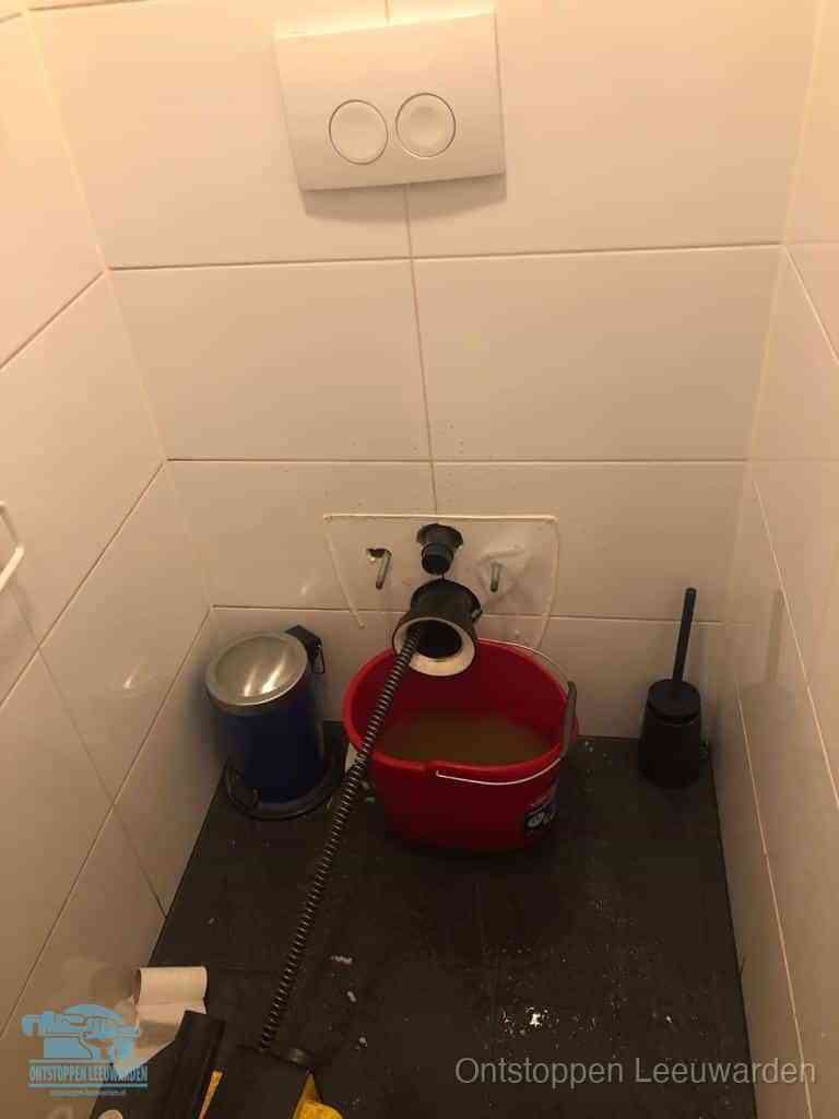 Een ontstopte wand-wc met verwijderde toiletpot waar een ontstoppingsveer in de wanduitgang verdwijnt, het achterhalen waar de verstopping zit in Leeuwarden
