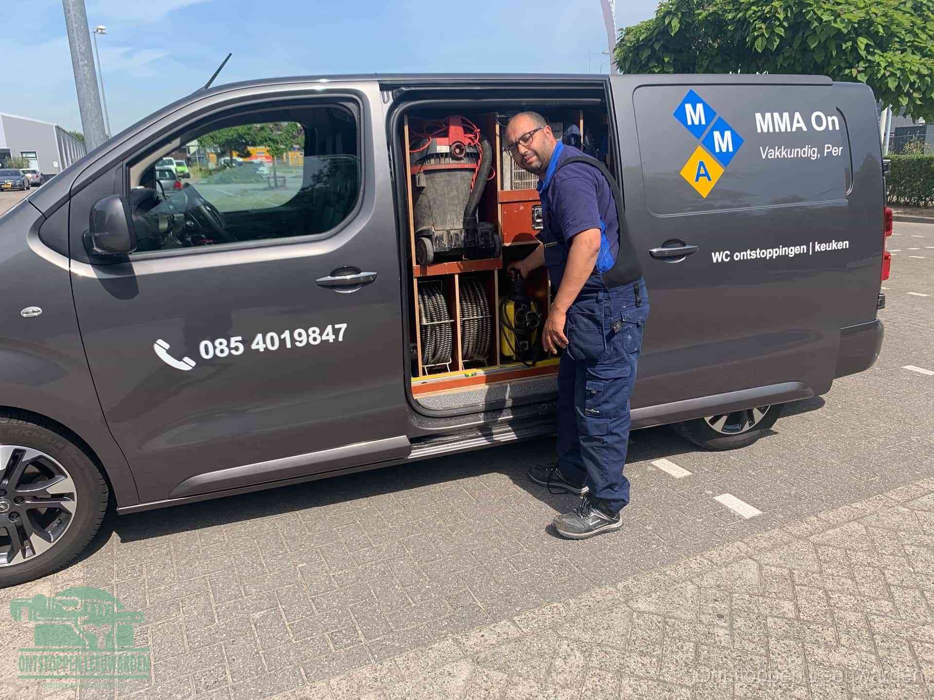 Een monteur bij de open schuifdeur van zijn bedrijfsbus op een parkeerplaats, klaar om de oorzaak van terugkerende afvoerverstoppingen aan te pakken in Leeuwarden