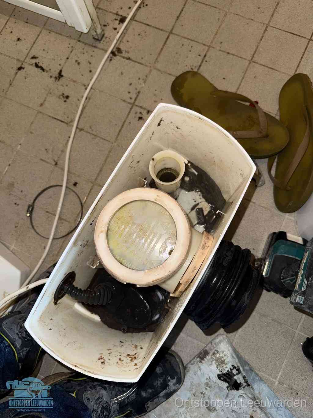 Een gedemonteerde toiletpot op de vloer met ontstoppingsveer en gereedschap ernaast, het verwijderen van een vastzittend voorwerp uit de wc in Leeuwarden