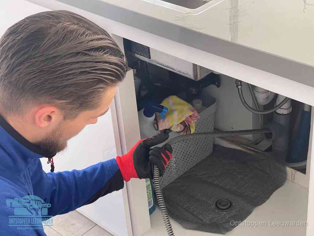 Een monteur voert een flexibele ontstoppingsveer in de afvoer om een verstopping voorbij de bocht van het toilet te bereiken in Leeuwarden
