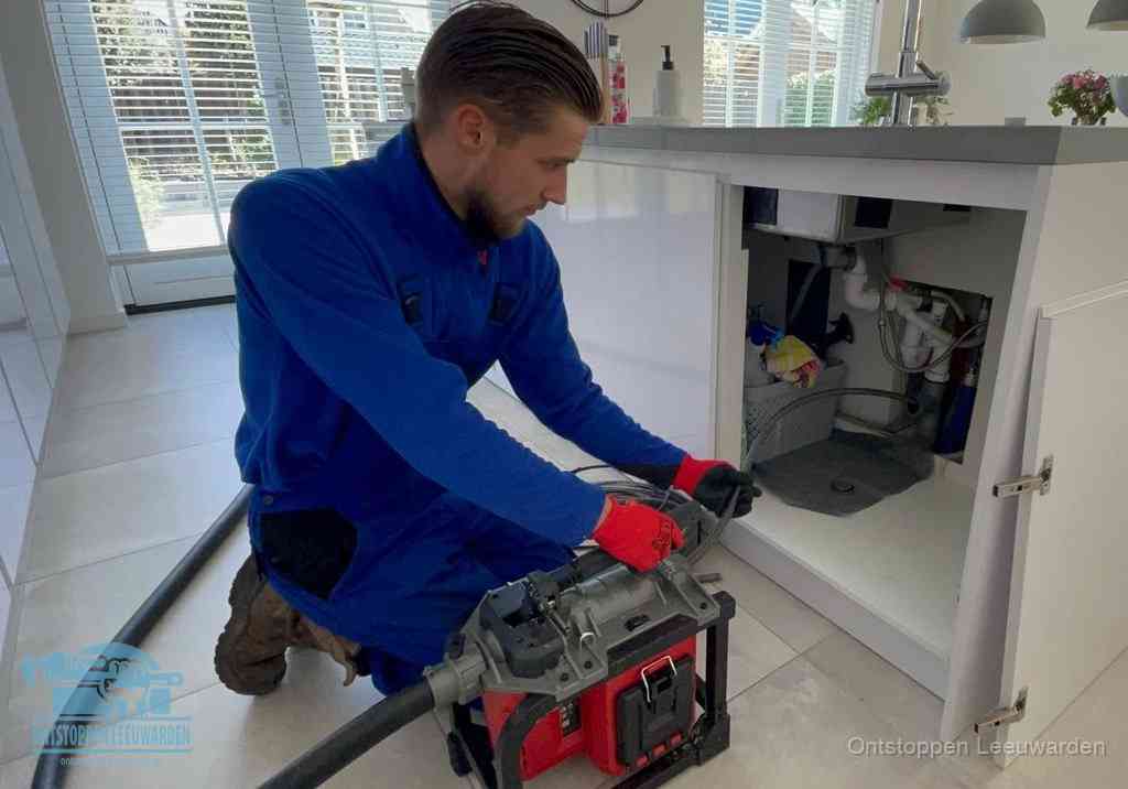Een monteur voert een professionele elektrische ontstoppingsmachine in de afvoer onder de spoelbak tijdens het gootsteen ontstoppen in Leeuwarden