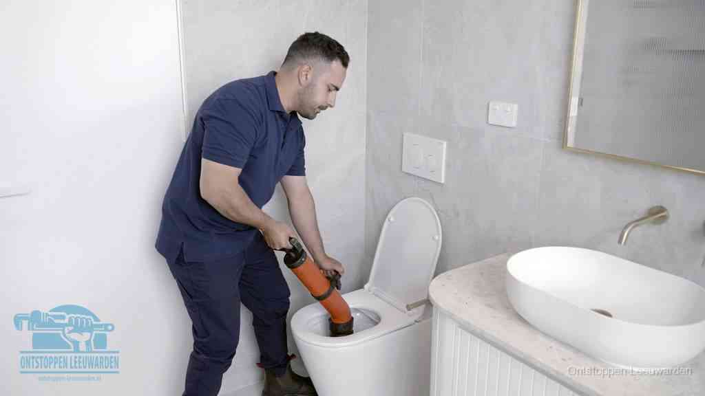 Een man gebruikt een handmatige luchtdruk-ontstopper in een modern betegeld toilet om zelf de wc te ontstoppen in Leeuwarden
